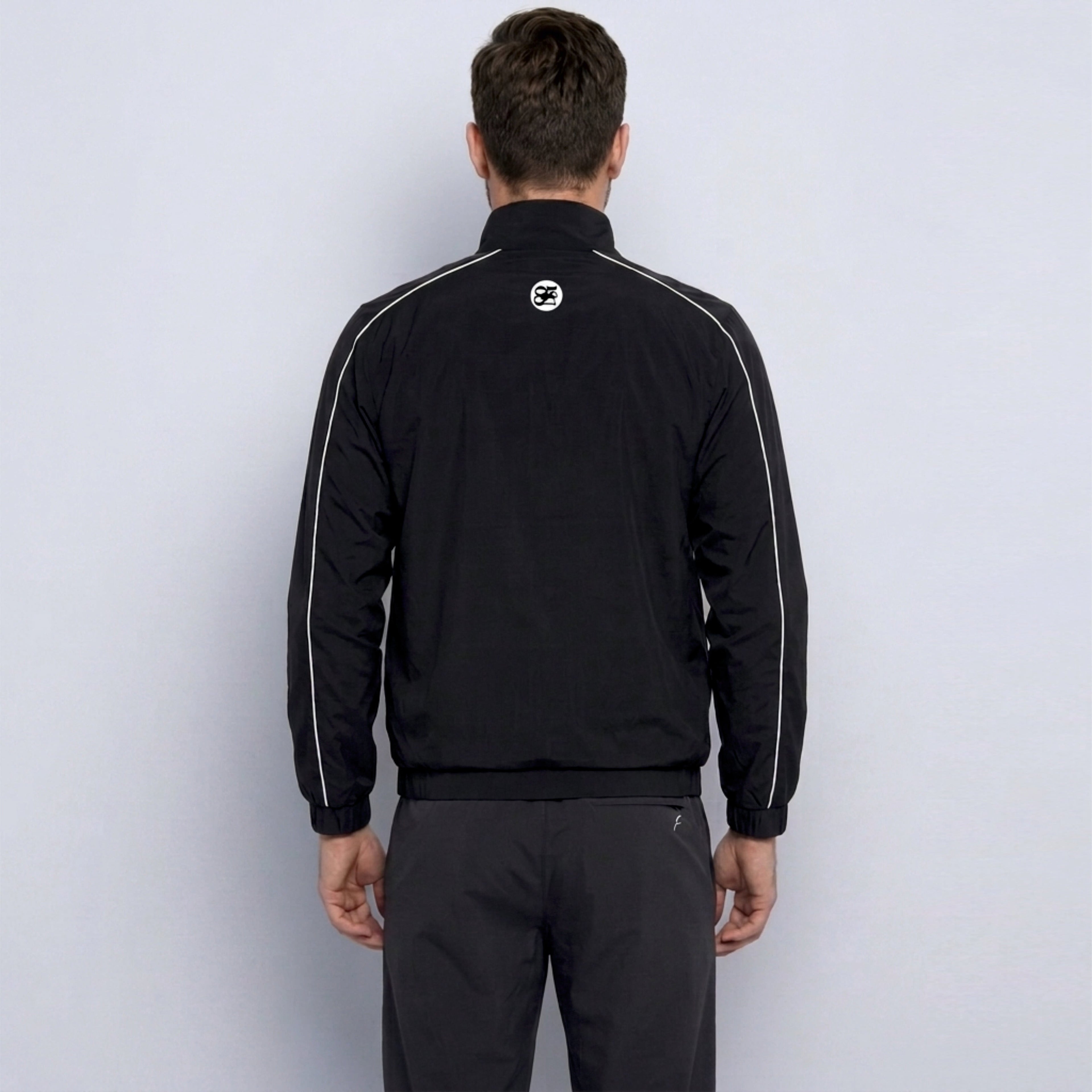 Person wearing a black tracksuit with a logo on the back against a white background