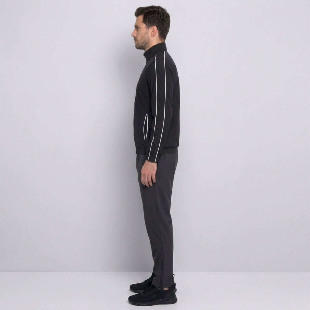 Man wearing a black tracksuit with white zippers against a light gray background