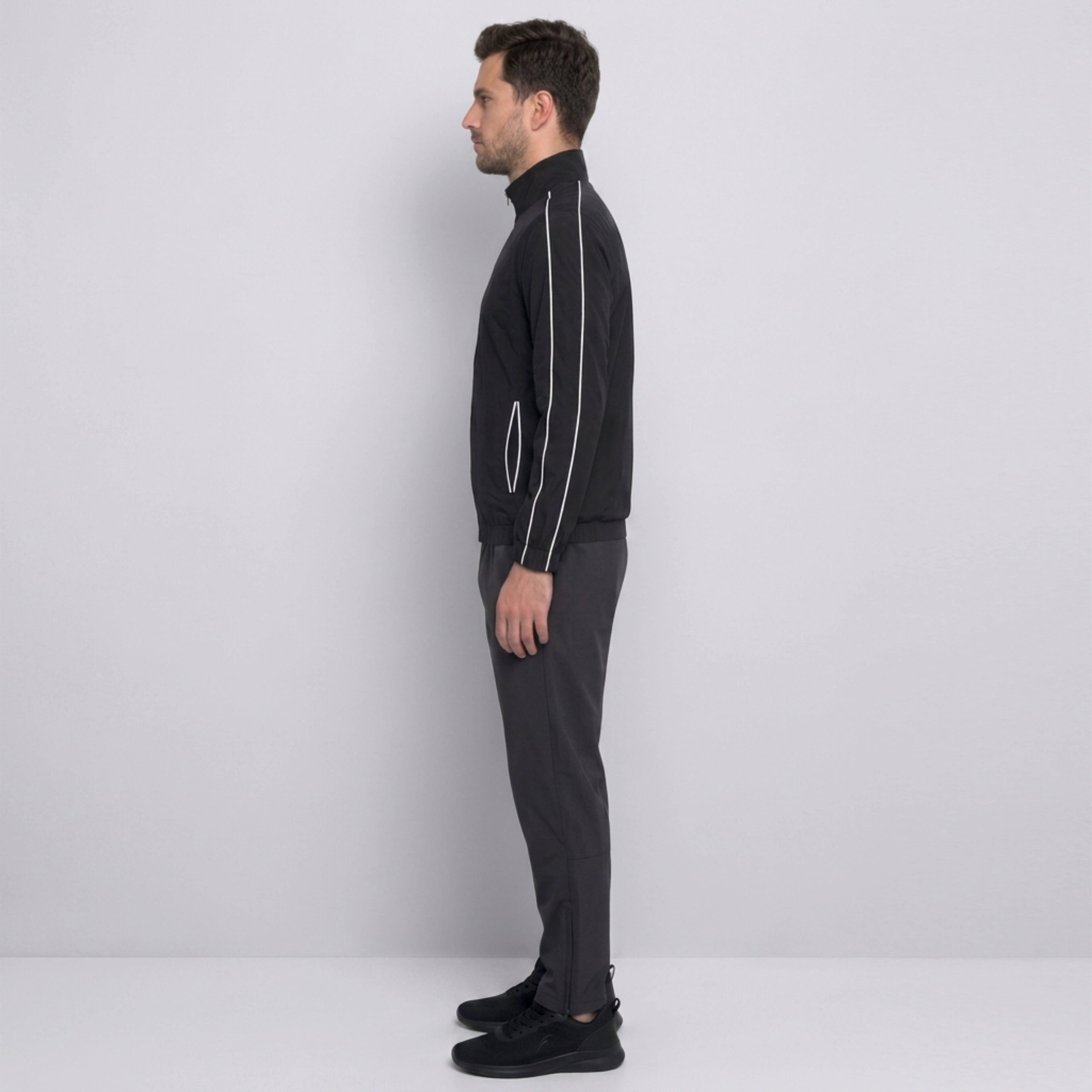 Man wearing a black tracksuit with white zippers against a light gray background