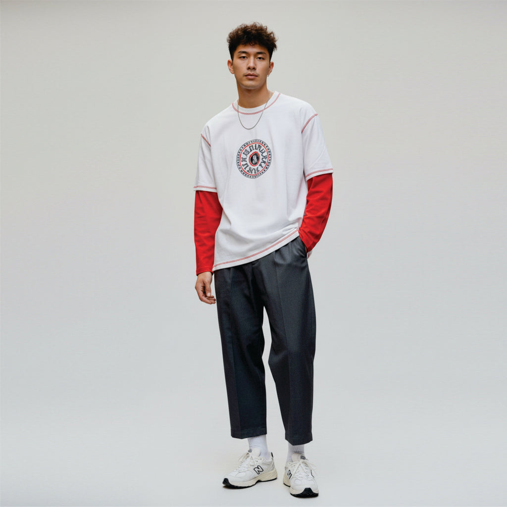Person wearing a white and red long-sleeve shirt with a graphic design, dark pants, and white sneakers on a light gray background.