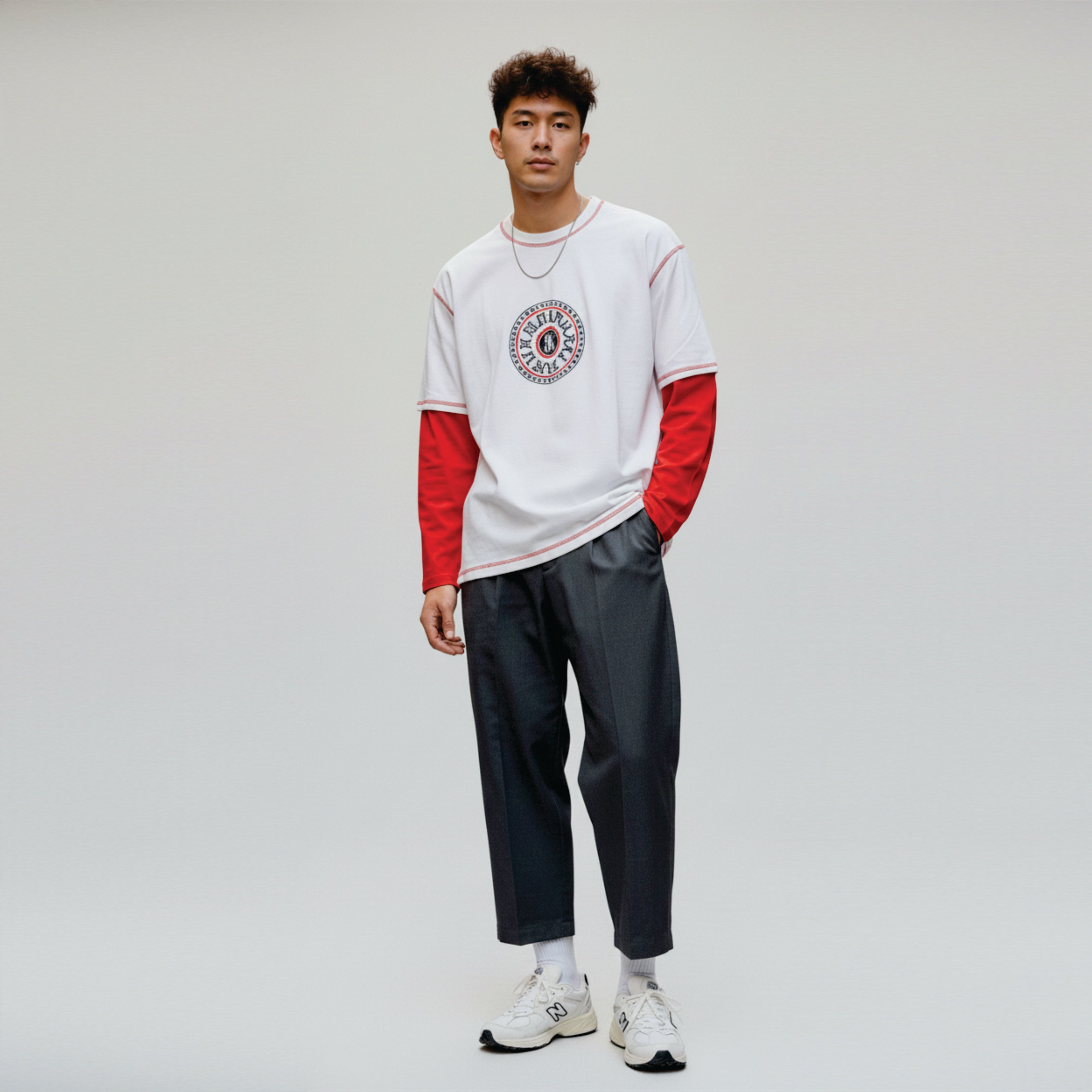 Person wearing a white and red long-sleeve shirt with a graphic design, dark pants, and white sneakers on a light gray background.