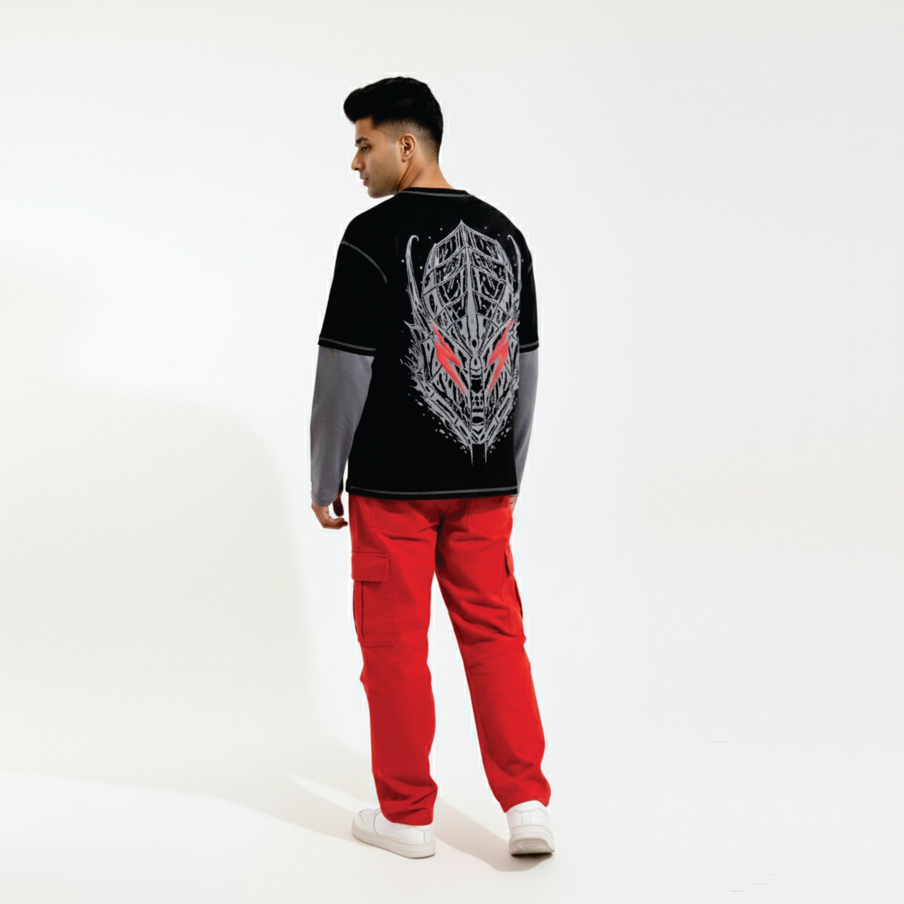 Person wearing a black long-sleeve shirt with a graphic design and red pants on a white background