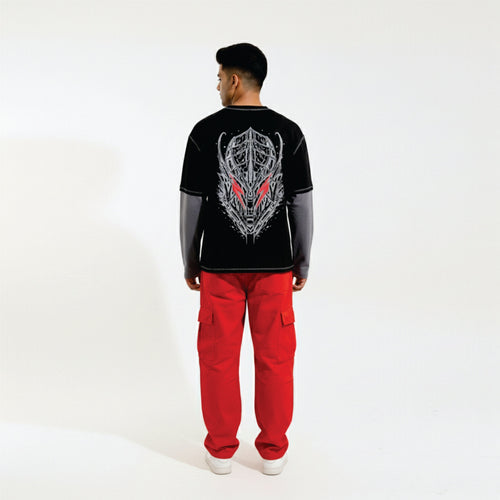 Person wearing a black long-sleeve shirt with a graphic design and red pants on a white background